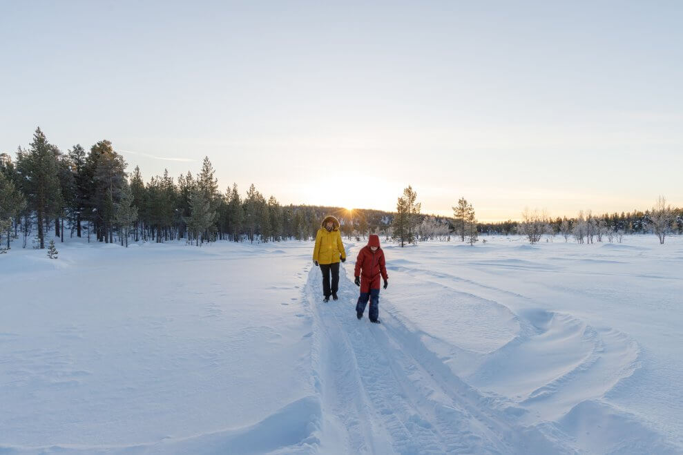 A parent and their child walk together along a snowmobile trail in the winter.