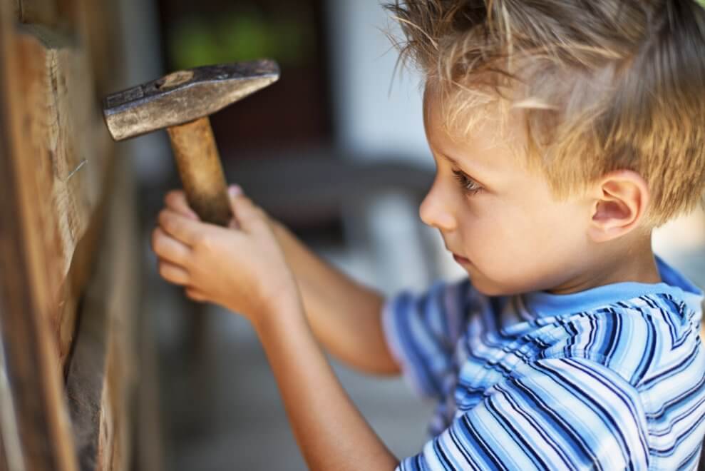 A young boy carefully uses a hammer to put a nail into a piece of wood.