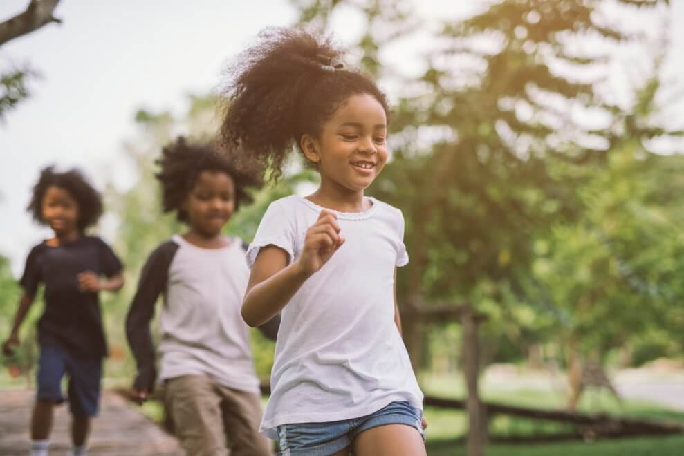 Three children run outside together, demonstrating a fundamental movement skill.