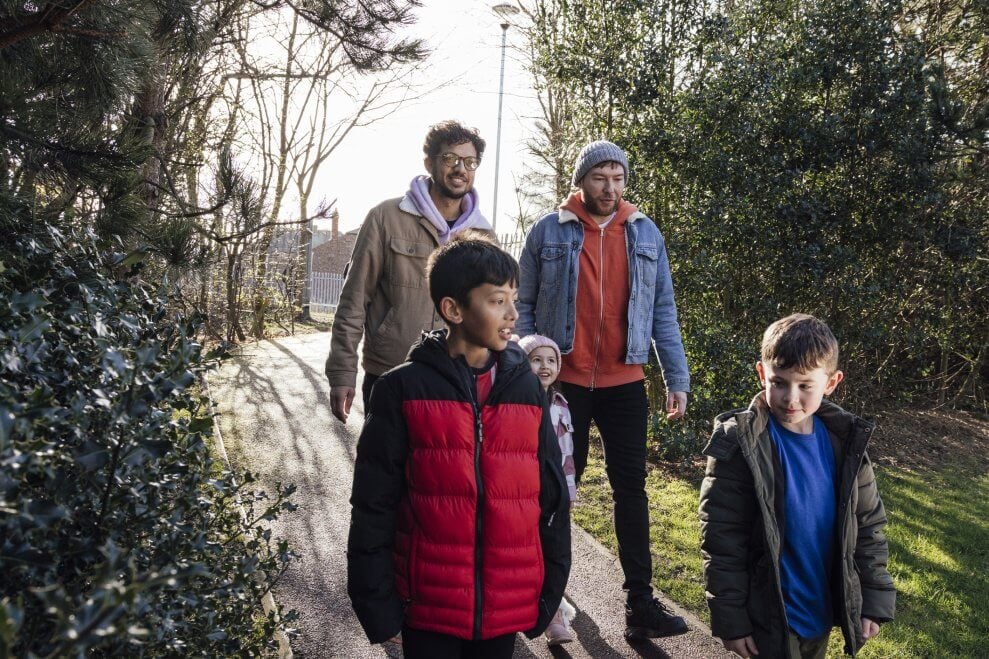 Two dads walk along a forested path with their three kids on a spring day. Spending active family time together is one way to help get kids more active.