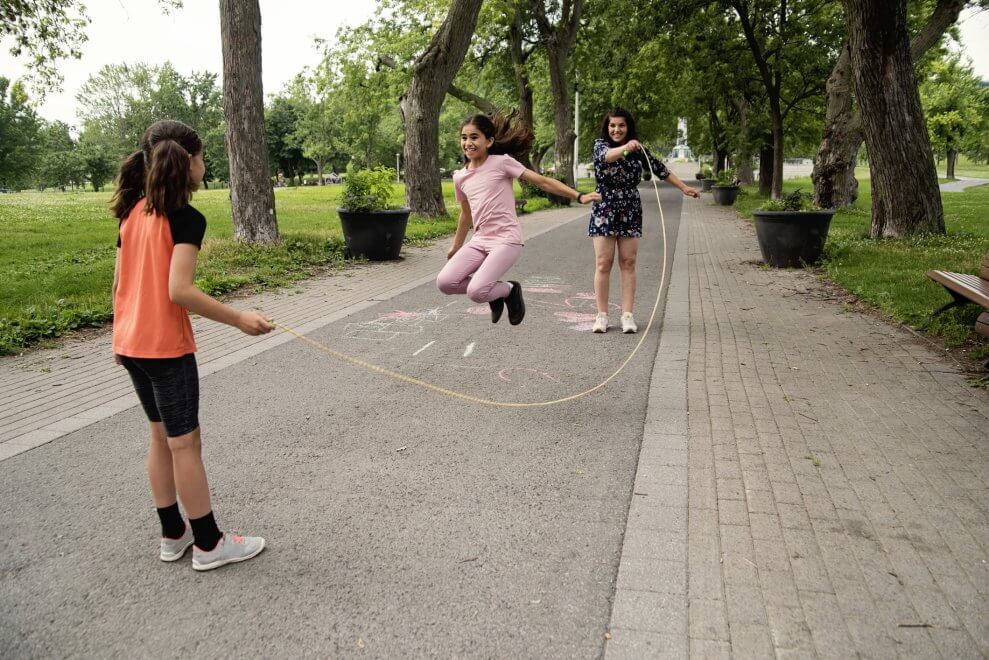 Two preteen girls play jump rope games with their mother.
