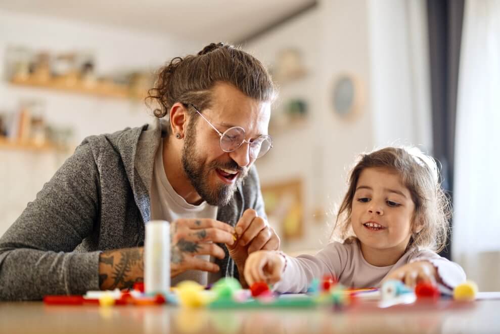 A father and his toddler daughter do crafts together at the kitchen table.