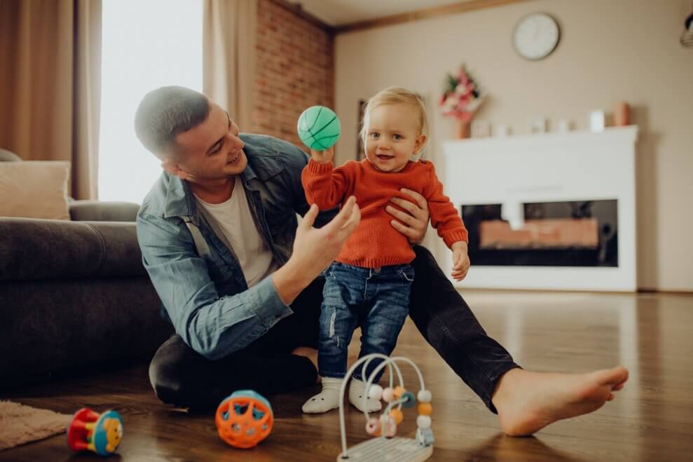 A father and his daughter play with a ball in their living room.