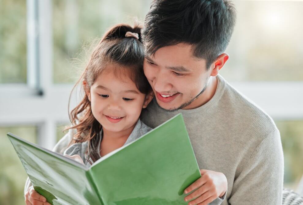A father and his toddler daughter read a book together at the library.