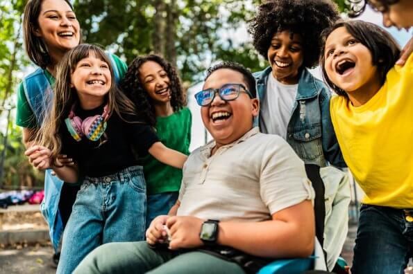 A group of children, including one in a wheelchair, laugh together outside.