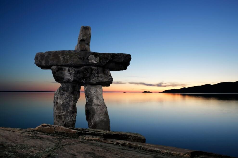 An inuksuk overlooks a lake at dusk. Building inuksuks is one example of a fun STEM activity for kids.