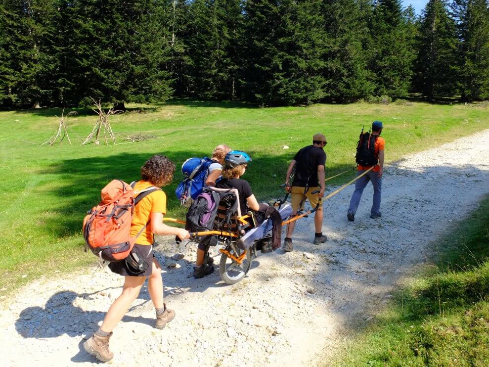 A group of people walk along a gravel path, assisting one person who's using a hiking wheelchair.