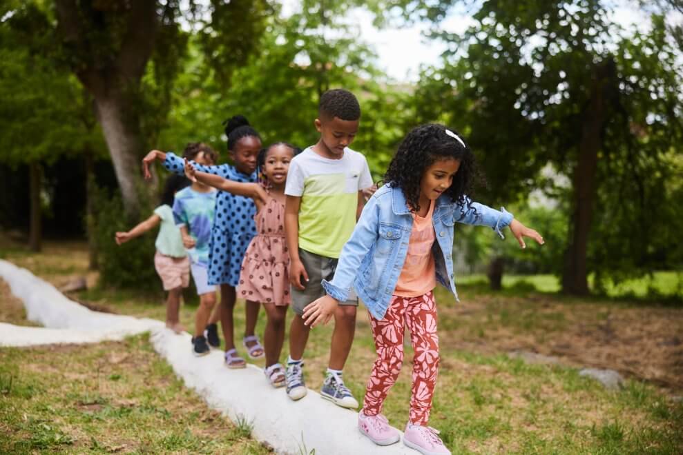 A group of children balance carefully as they walk across a log in single file.