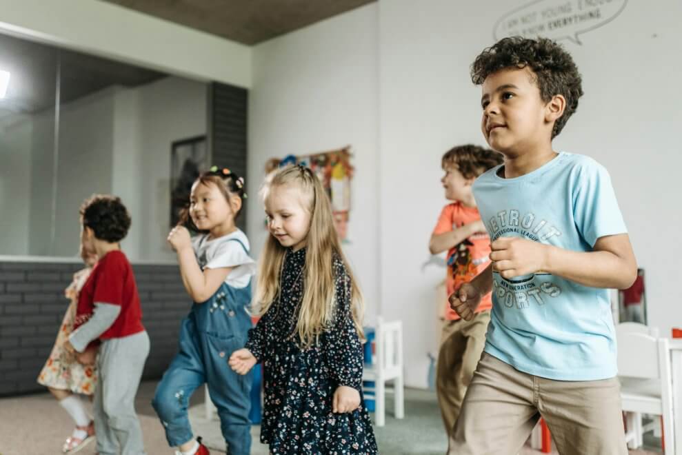 A group of young children dance and march together in a classroom. Teaching kids a pattern dance is one example of a STEM activity for kids.