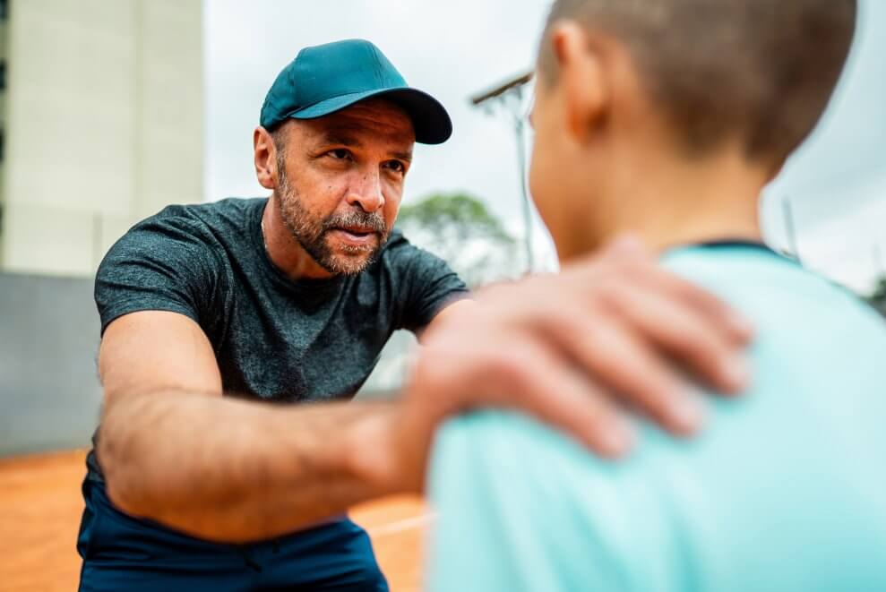 A coach talks to an athlete on the court, with his hands on the boy's shoulders.