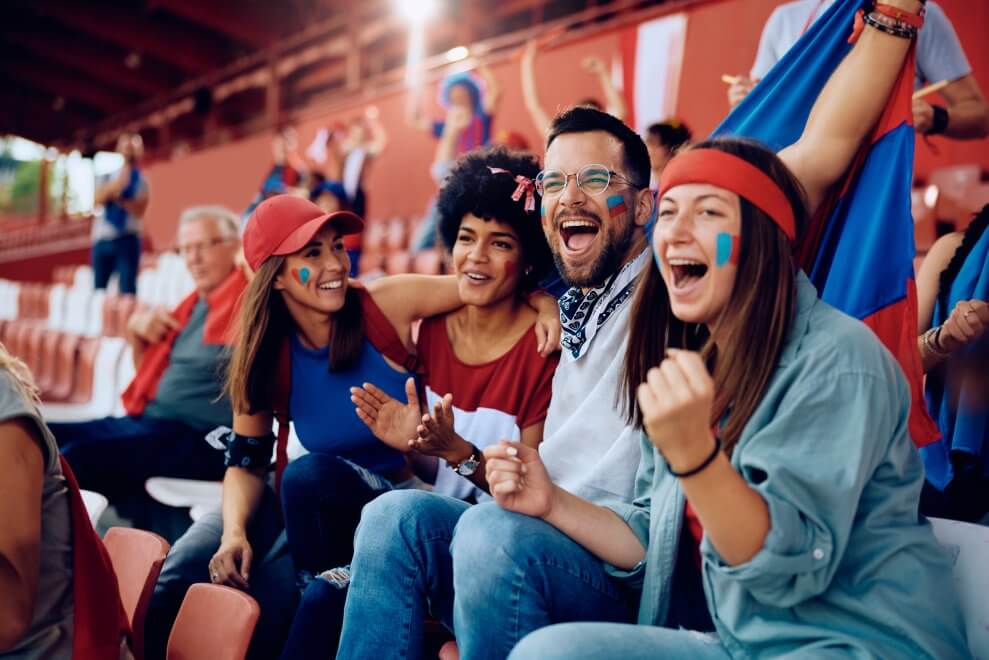 A group of sports parents cheers on the bleachers at a youth sports game.