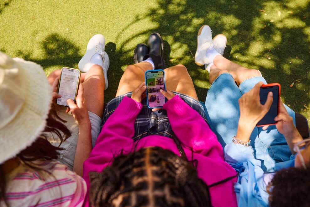 Three teenage girls sit outside, each using a smartphone.