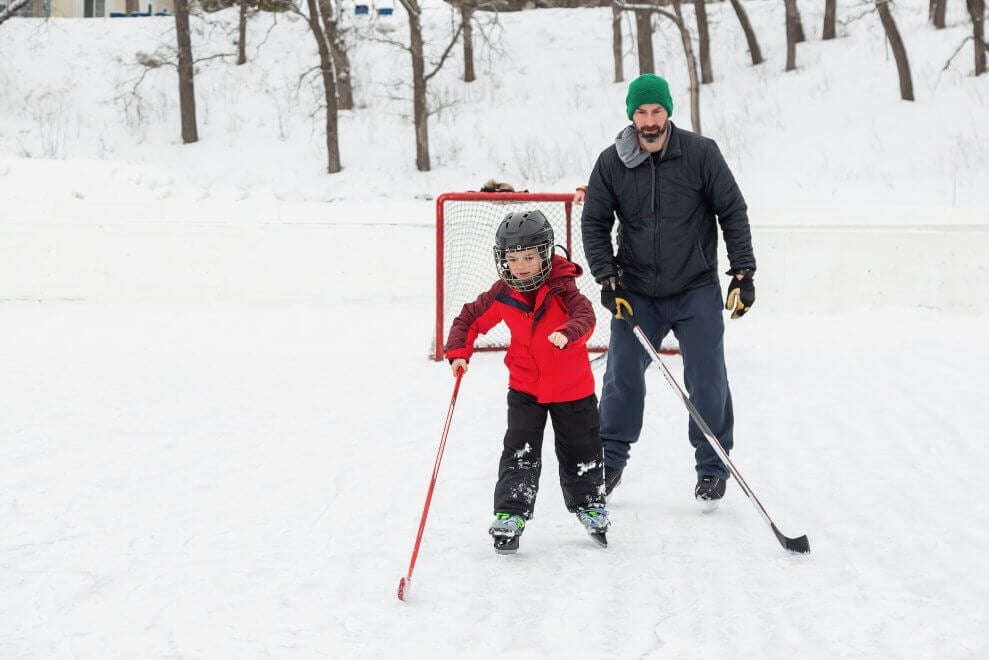 A young boy and his dad play hockey together on an outdoor rink.