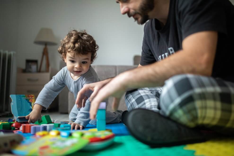 A father and his toddler son play with blocks in their living room.