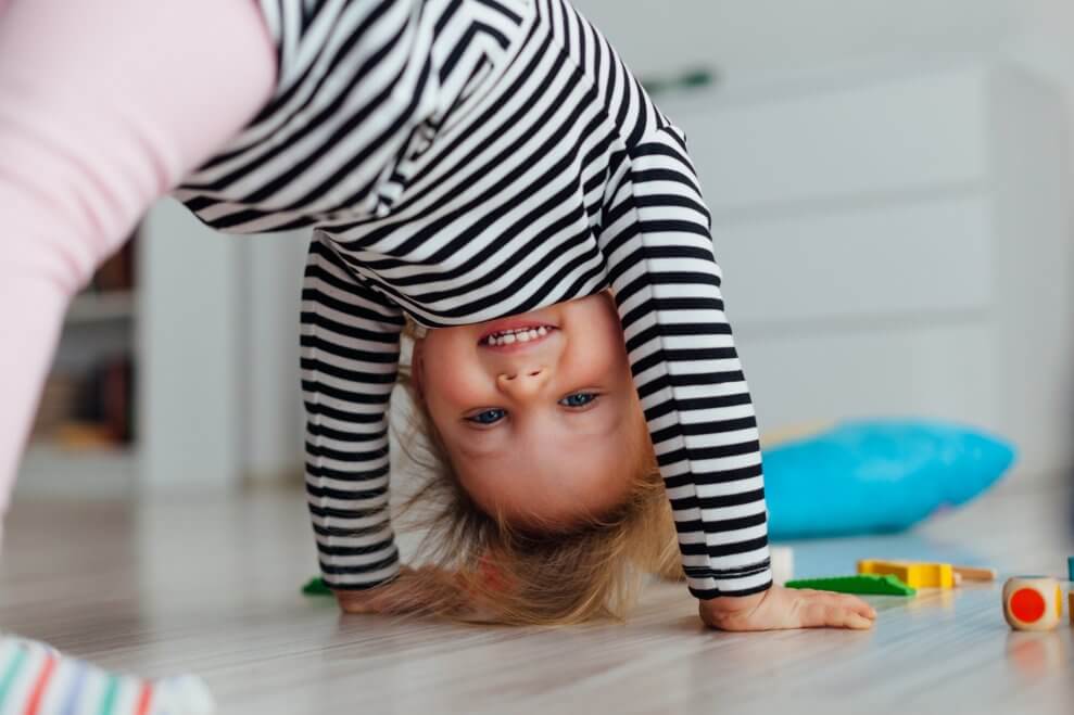 A toddler hangs out in downward dog with a smile on her face.