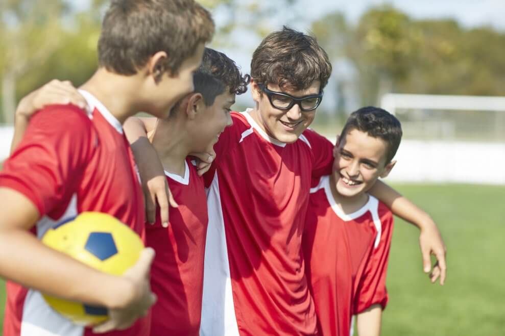 Four preteen boys walk together on a soccer field after a game.