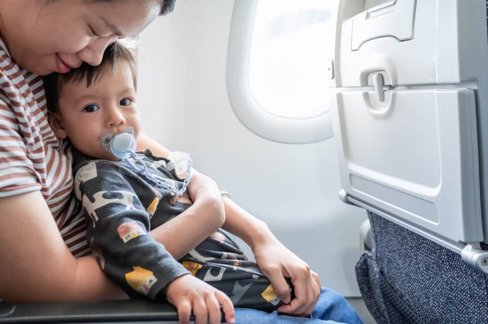 A smiling mom snuggles with her toddler on an airplane.