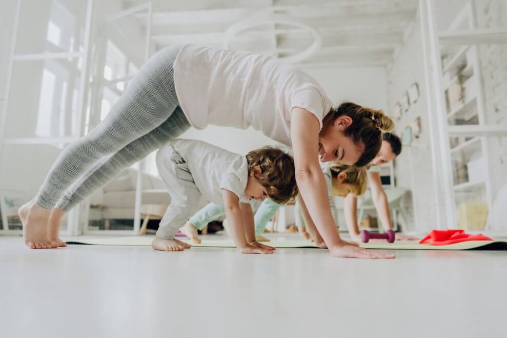 A mom, dad, and their two kids—one of whom is a toddler—do yoga together in their living room.