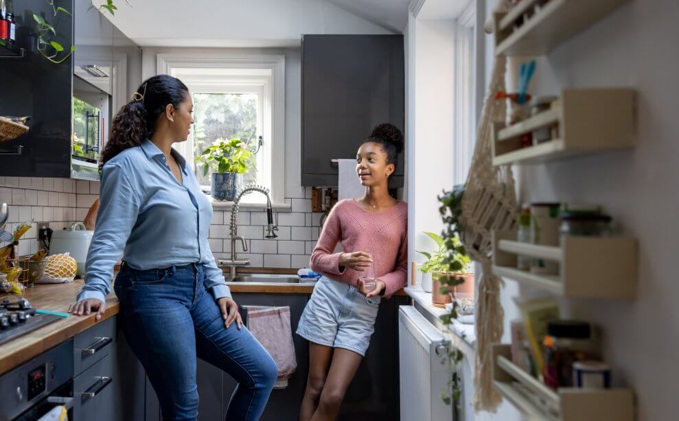 A mom and her teenage daughter talk in the kitchen.