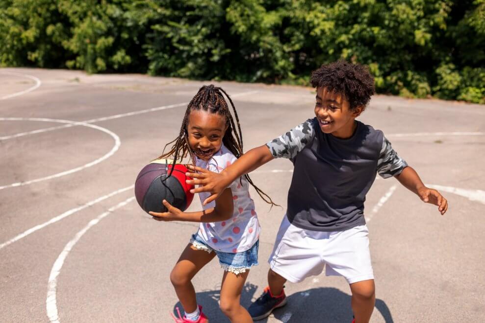 A boy and a girl play basketball on an outdoor court.