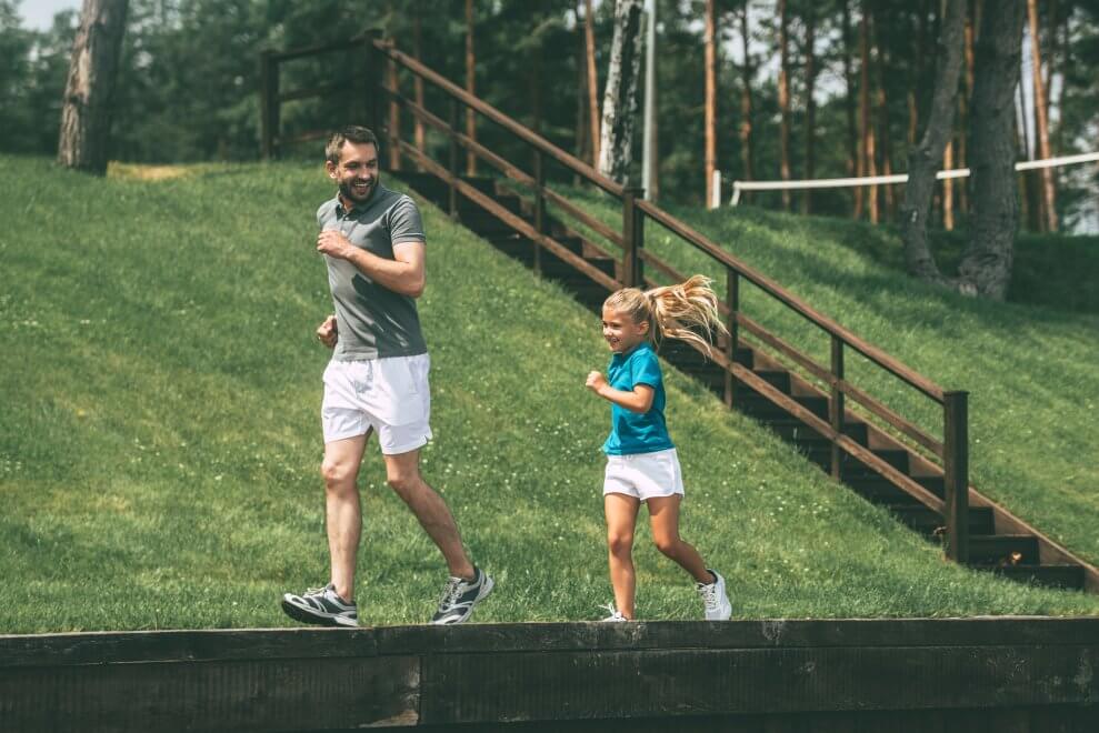 A dad and his daughter run together on a summer day.