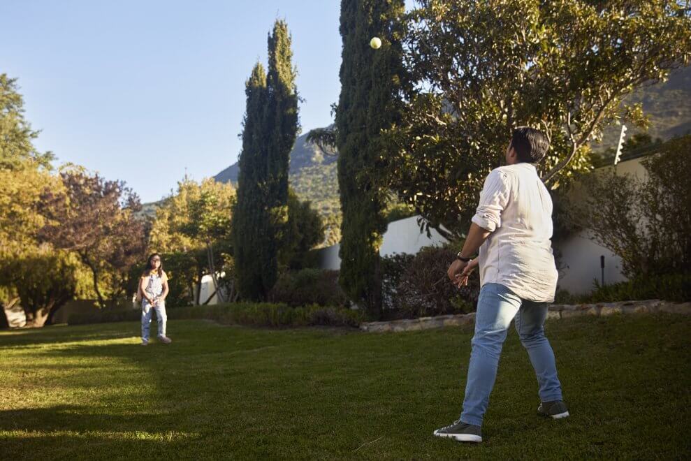 A father and his daughter play catch with a tennis ball in their backyard.