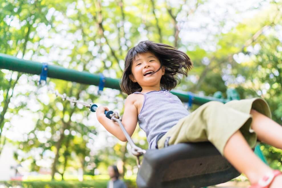 A girl swings on a swing at the playground on a summer day. She has a big smile on her face.
