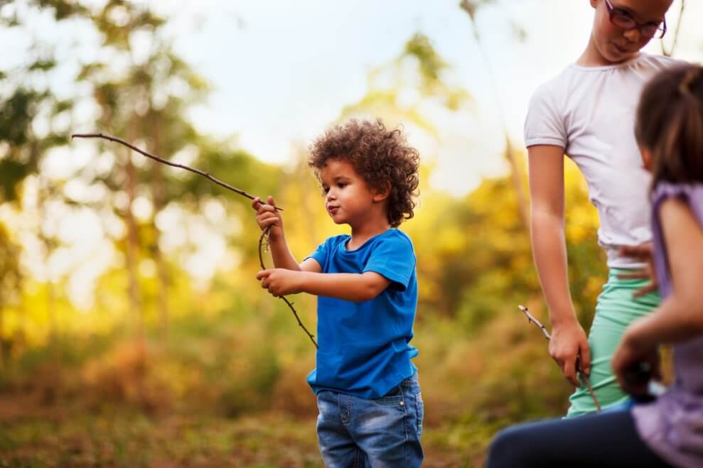 A boy plays with a stick outdoors, alongside some other children.