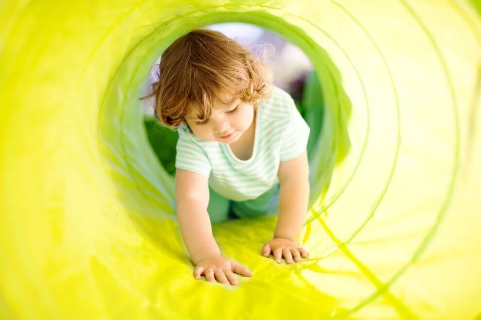 A toddler crawls through a bright green tunnel.
