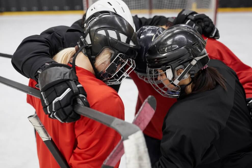A group of female hockey players huddle on the ice.
