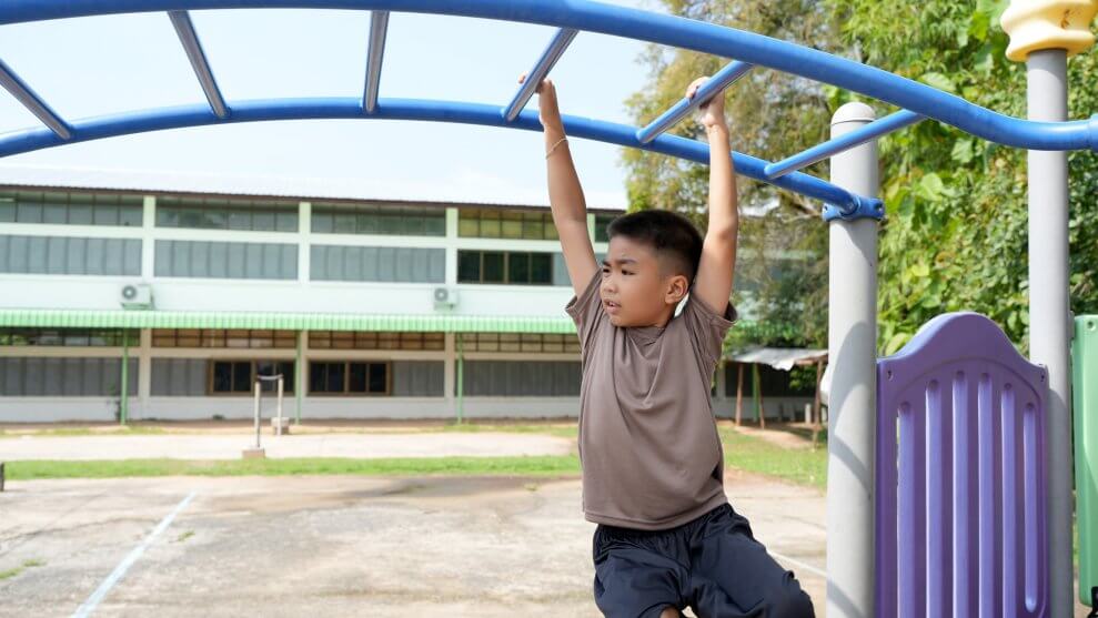 A boy swings across the monkey bars at a playground. He has a look of concentration on his face.
