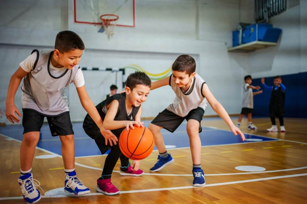 A group of elementary-age boys plays basketball in a gymnasium.