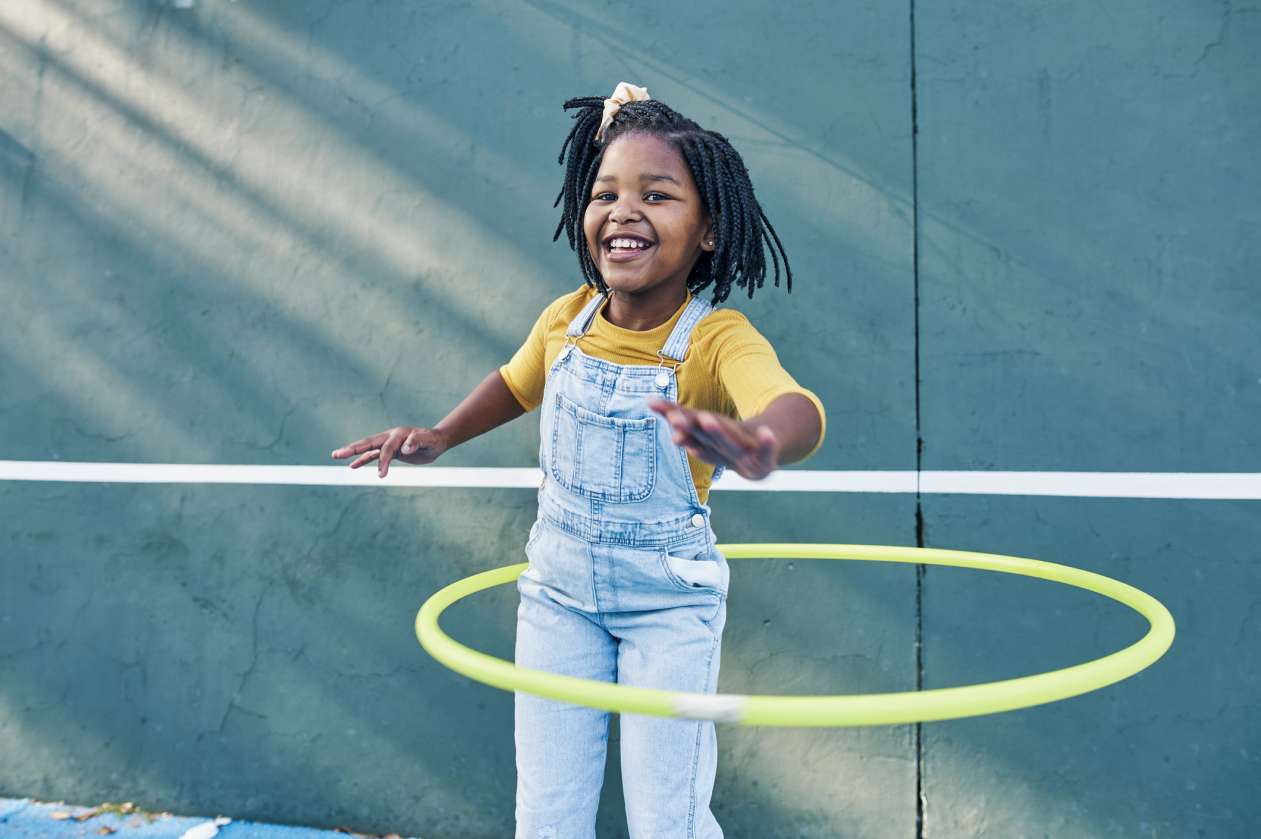 A little girl hula hoops outside with a smile on her face.