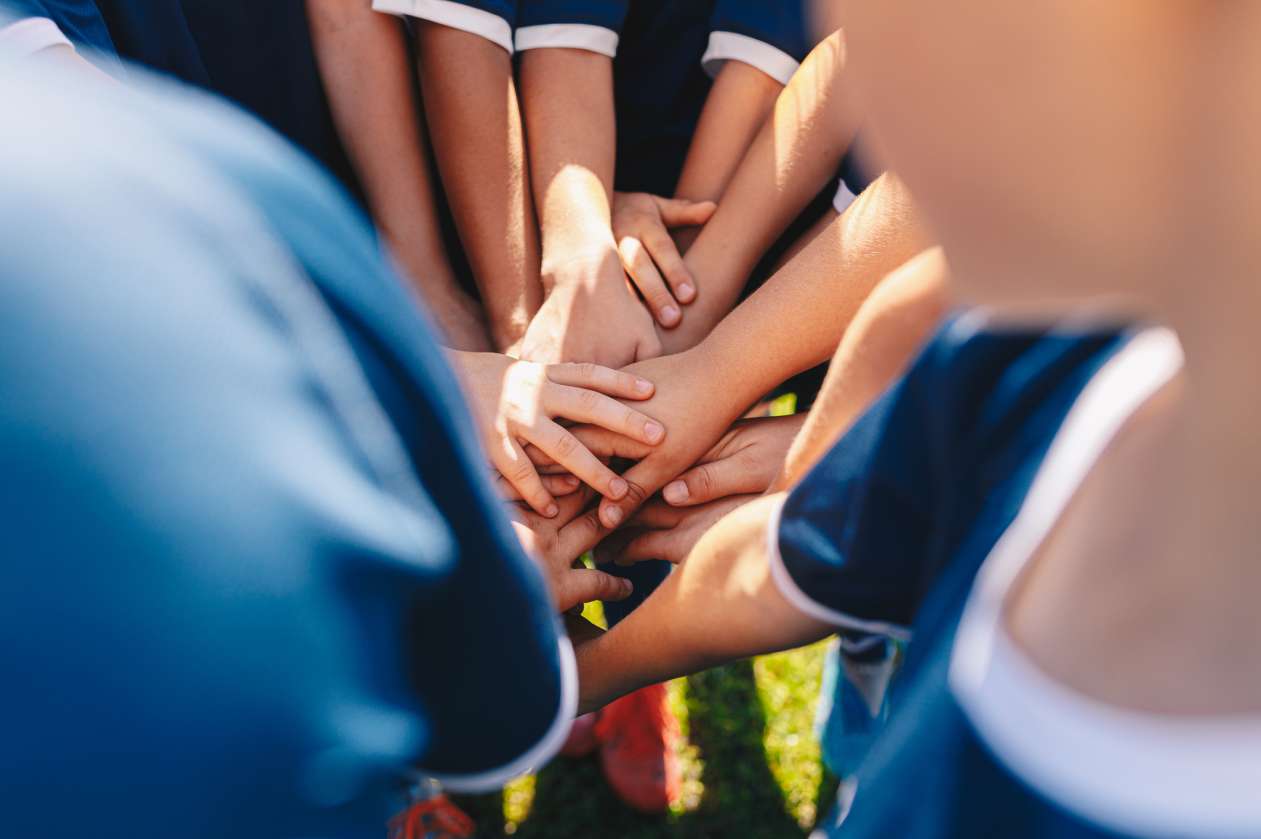 A group of children on a sports team stack their hands on top of each other during a team cheer.