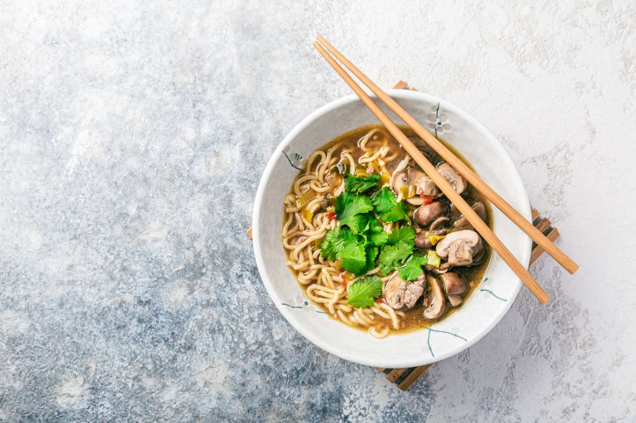 A bowl of miso ramen soup sits on a countertop with a pair of chopsticks resting on top of the bowl.