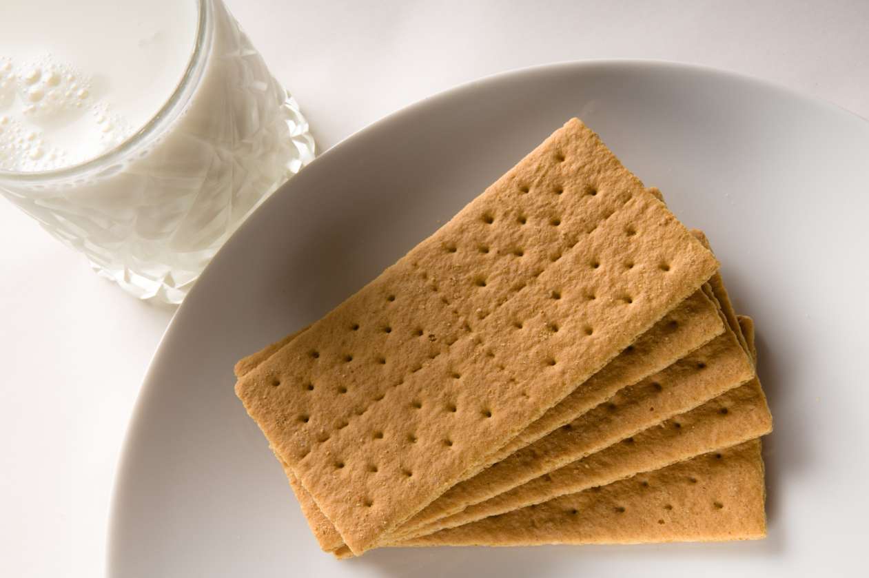 A glass of milk sits next to a plate of graham crackers.