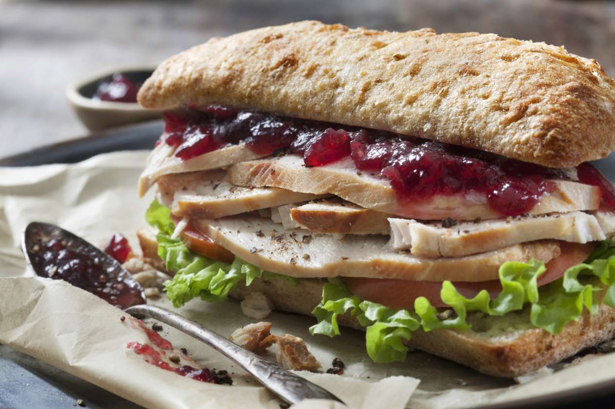 A sandwich on a platter is stuffed full of leftover turkey, cranberry sauce, and lettuce.