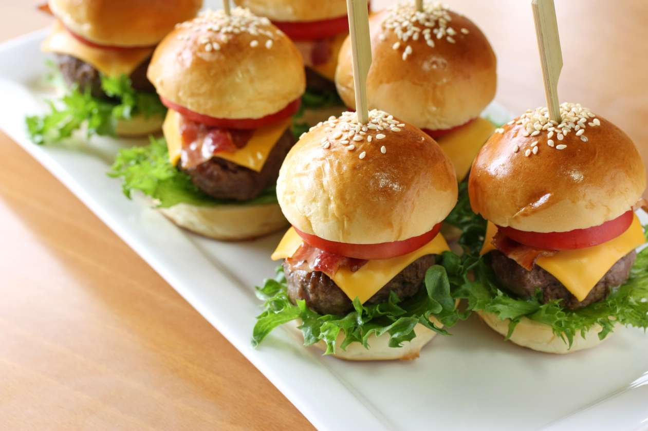 Small hamburgers sit on a serving tray.