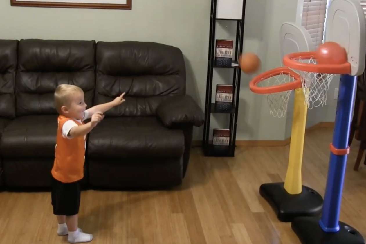 Titus the toddler shoots two balls into two kid-sized basketball nets at the same time—and scores both.
