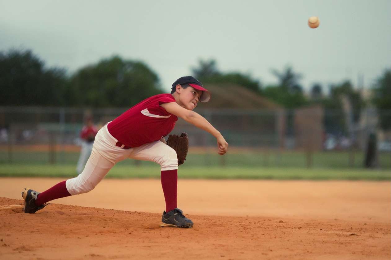 A boy stands on the pitcher's mound and throws a baseball towards home plate.