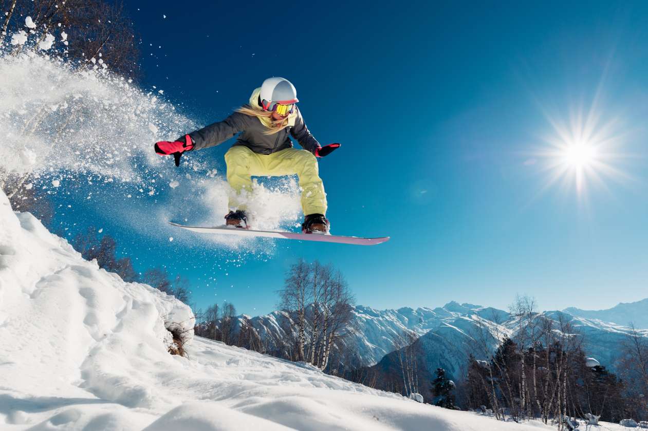 A woman snowboards in the mountains on a sunny day.