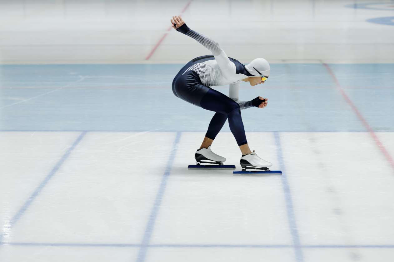An athlete speed skates around a rink.