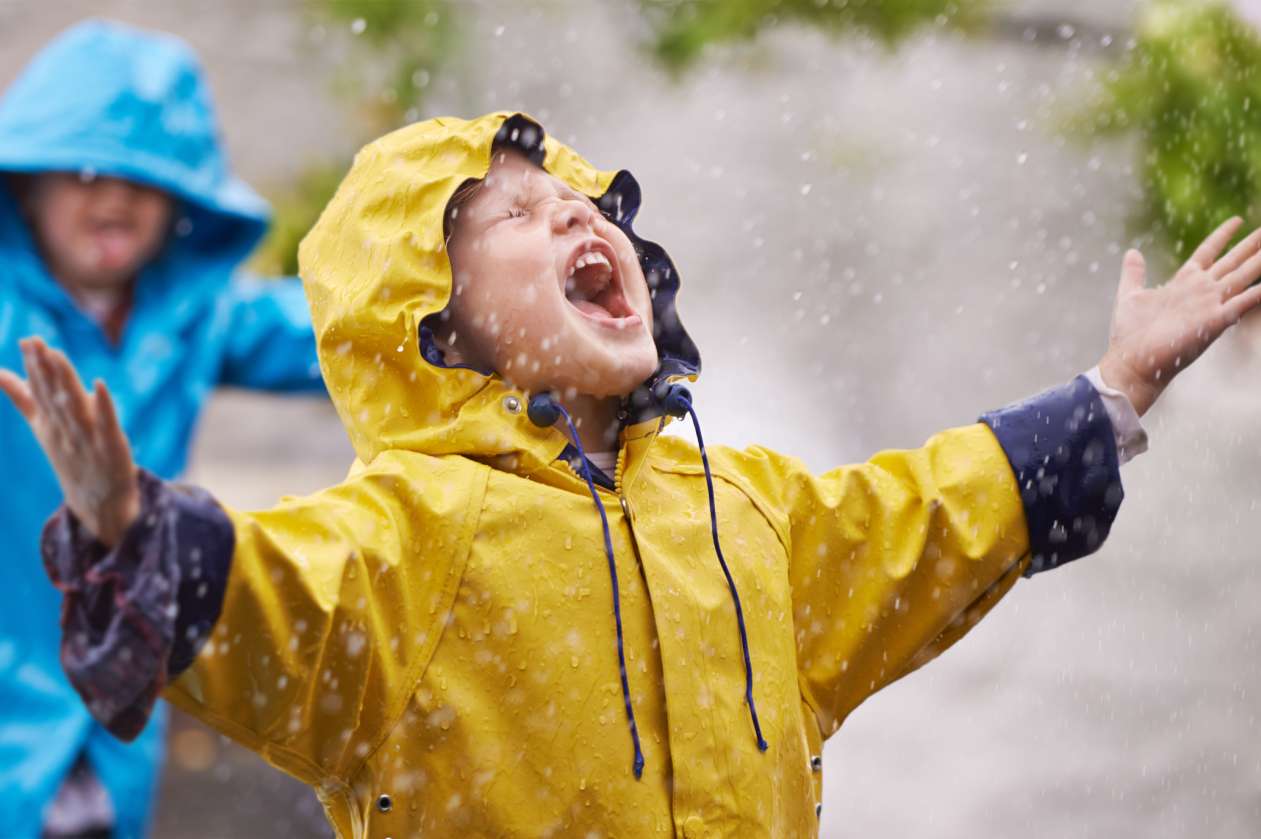 Two siblings happily playing in the rain, wearing rain suits