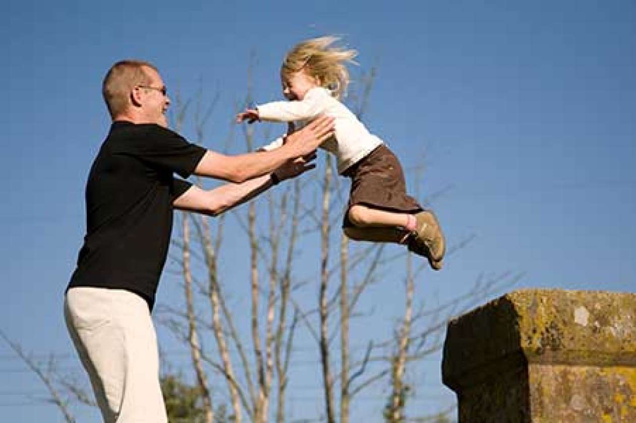 A dad helps his child jump from a pillar