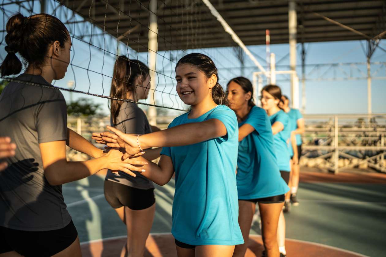 Two teams of preteen female volleyball players shake hands at the net.