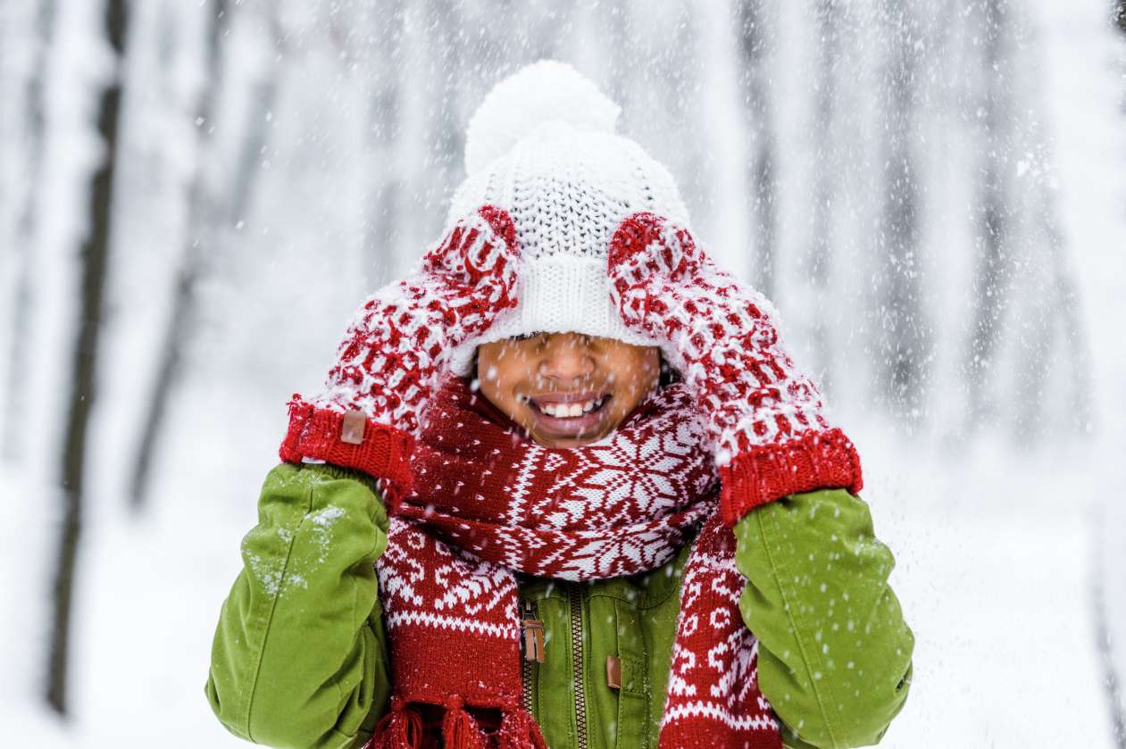 Child dressed for winter, wearing coat, hat, mitts, and scarf.