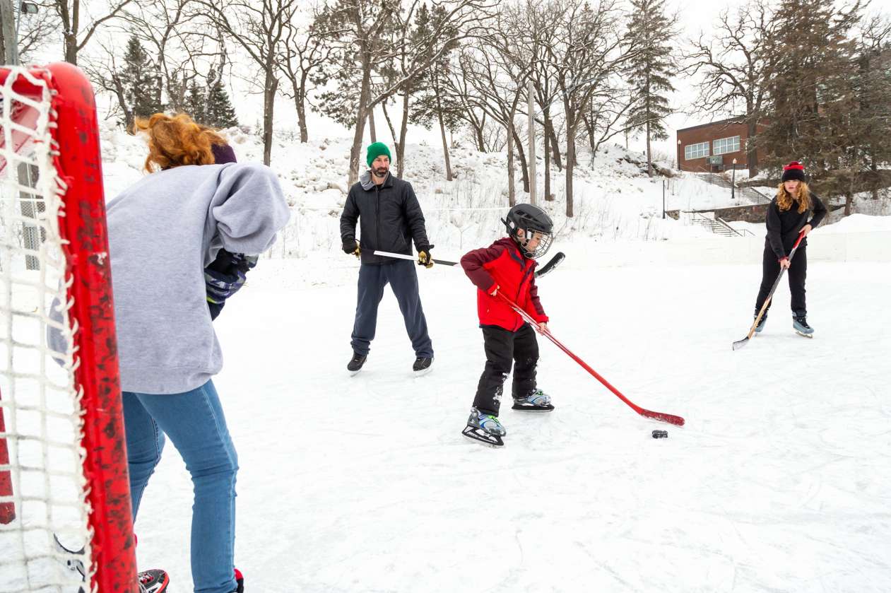 A mother, father, and their two kids play ice outdoors on a community rink.