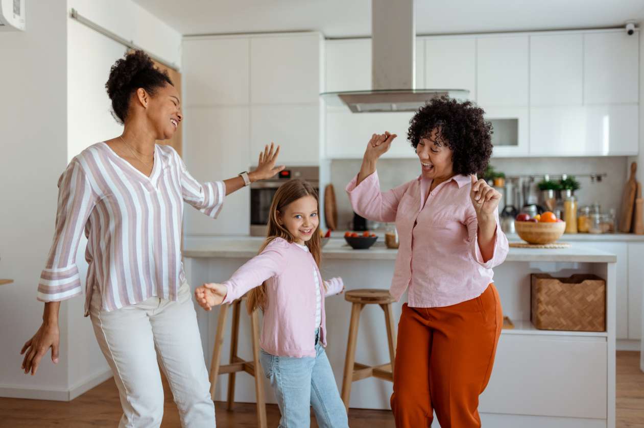 Two moms dance in the kitchen with their 