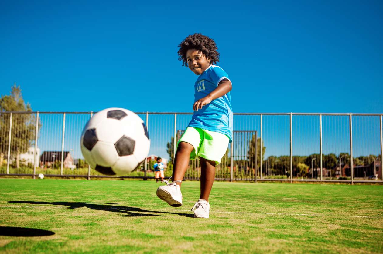 Child kicks a soccer ball on the field on a summer day