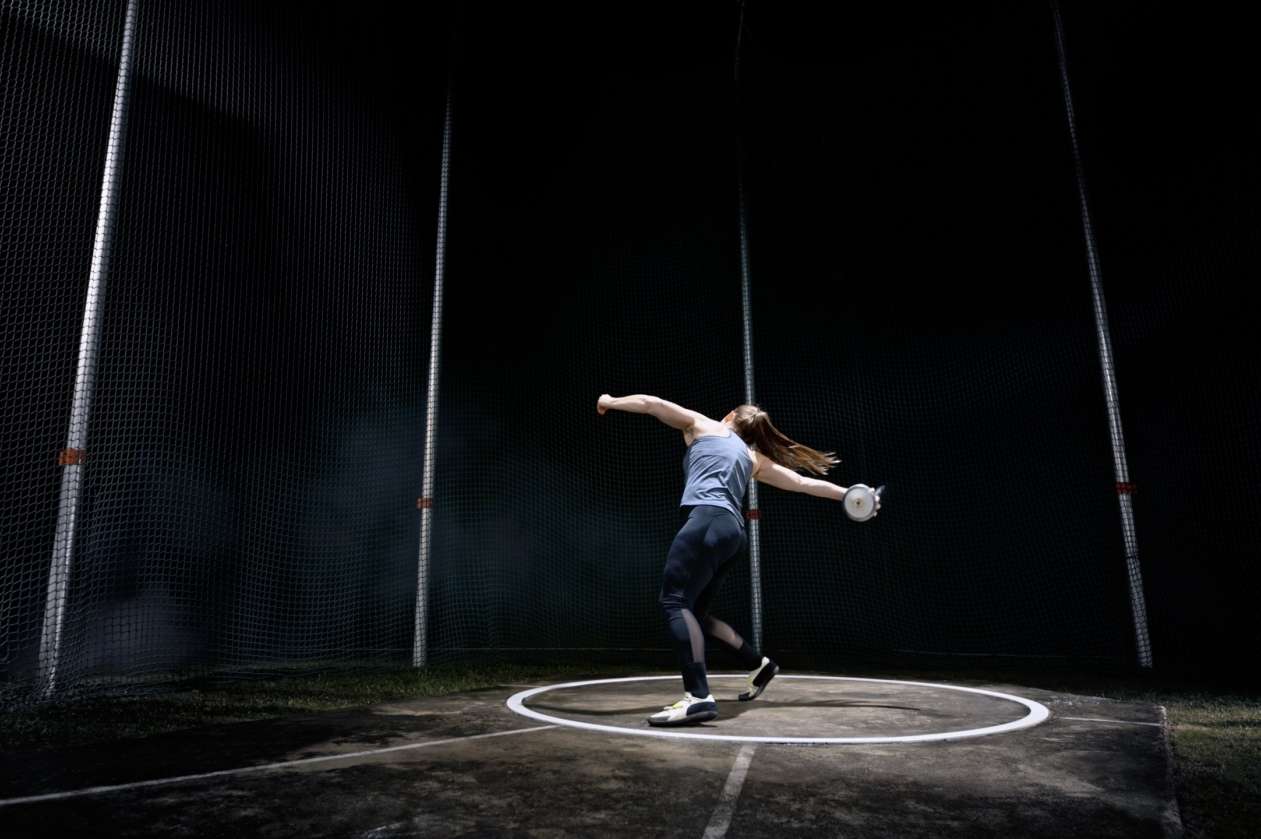 A woman prepares to launch a discus at nighttime on a field.